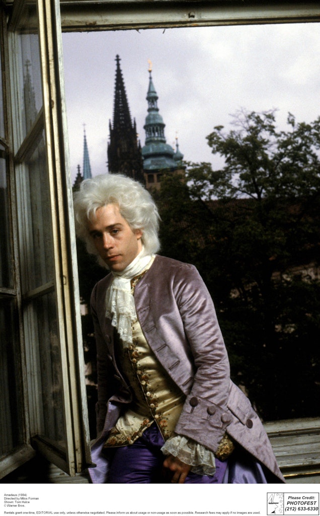 Man dressed as Mozart sitting on window sill with castle in background