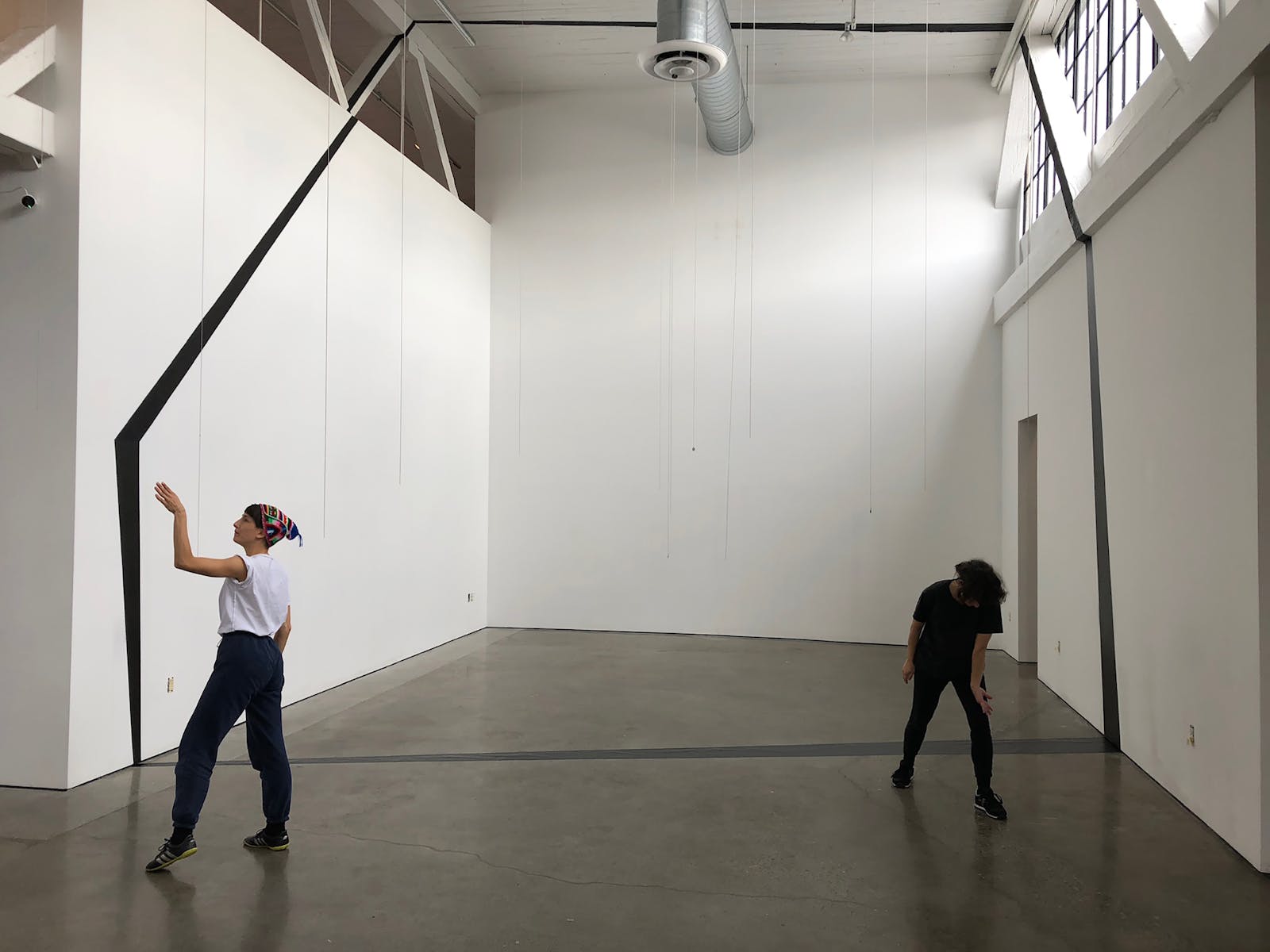 Two dancers in an empty room with large trapezoid shape taped onto the wall, floor, and ceiling