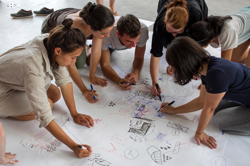 A group of adults write on a large piece on paper on the floor.