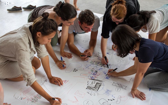A group of adults write on a large piece on paper on the floor.