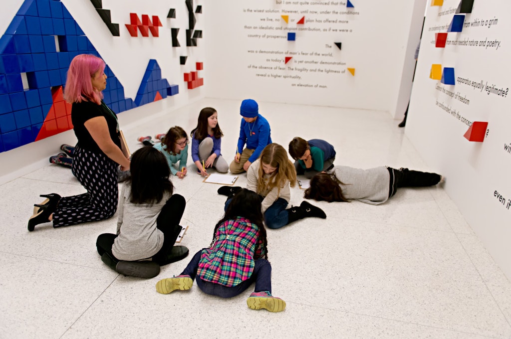 Kids sitting on floor in circle in front of art.