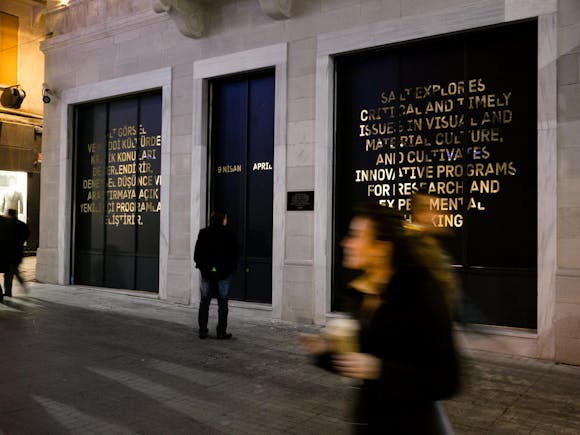 People walk past words printed in gold on the outside of a building.