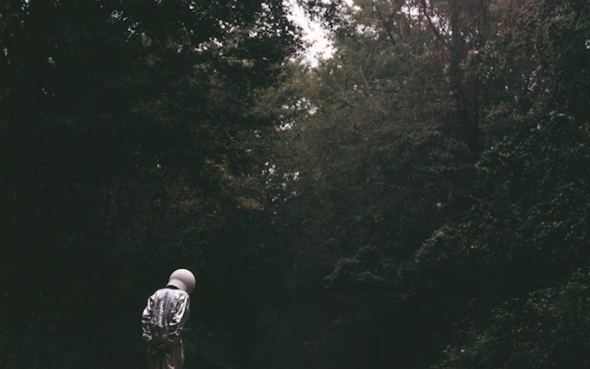 Man in space suit on a dirt road in woods.