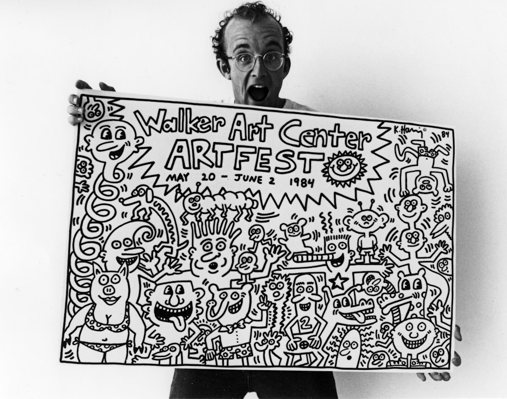 A man yells with joy at the veiwer while holding a poster filled with cartoon like illustrations and the title 