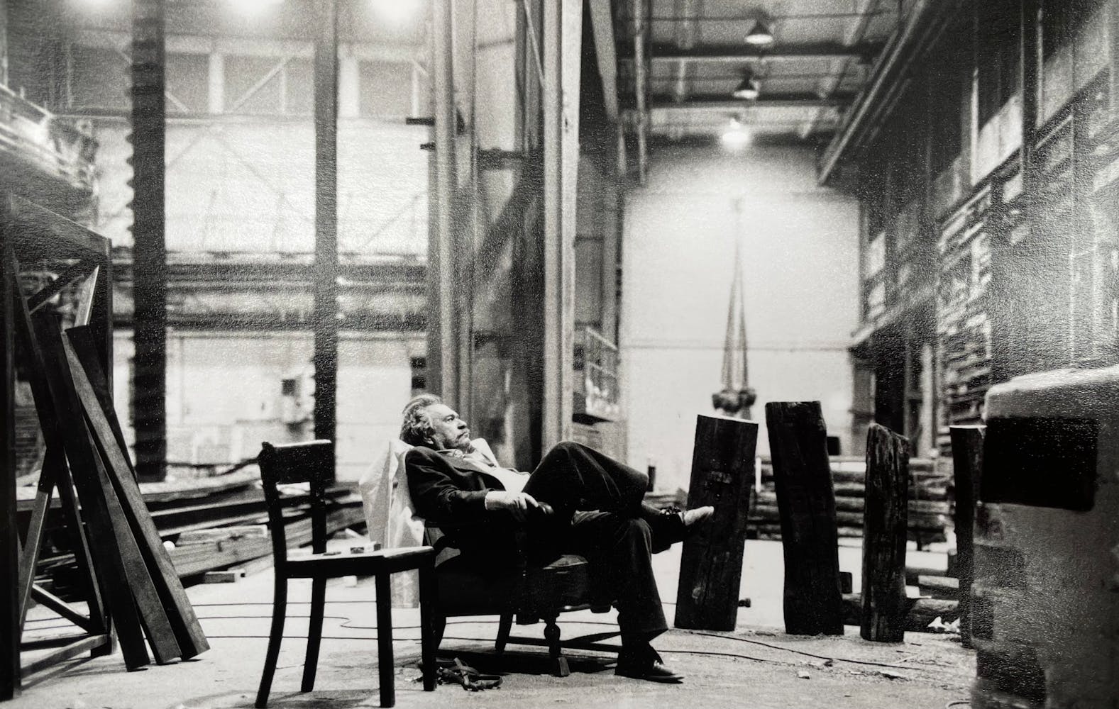 A man in a suite sits in a chair in a gallery that is under construction.