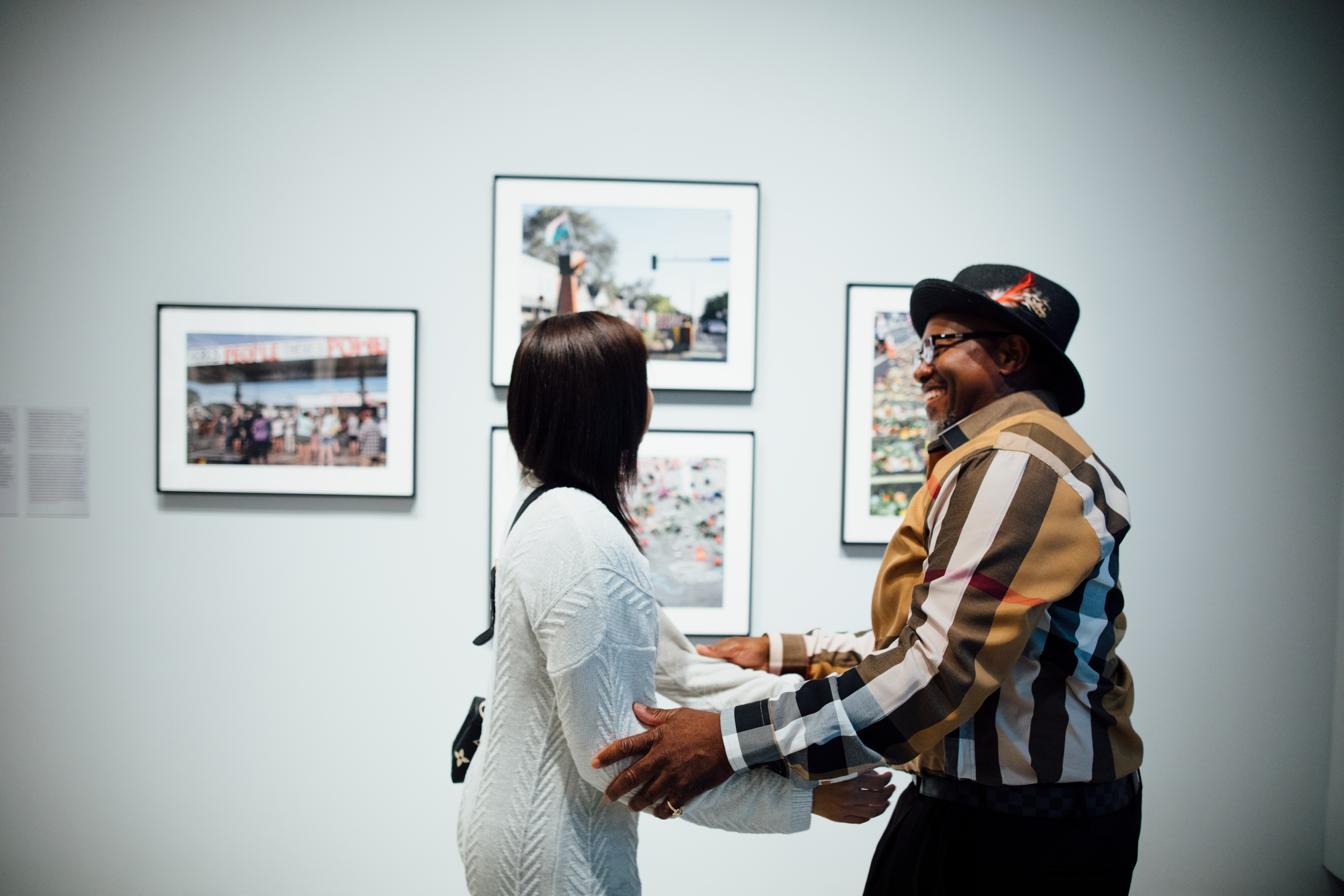 Two people smile and greet each other in a gallery in front of photographs.