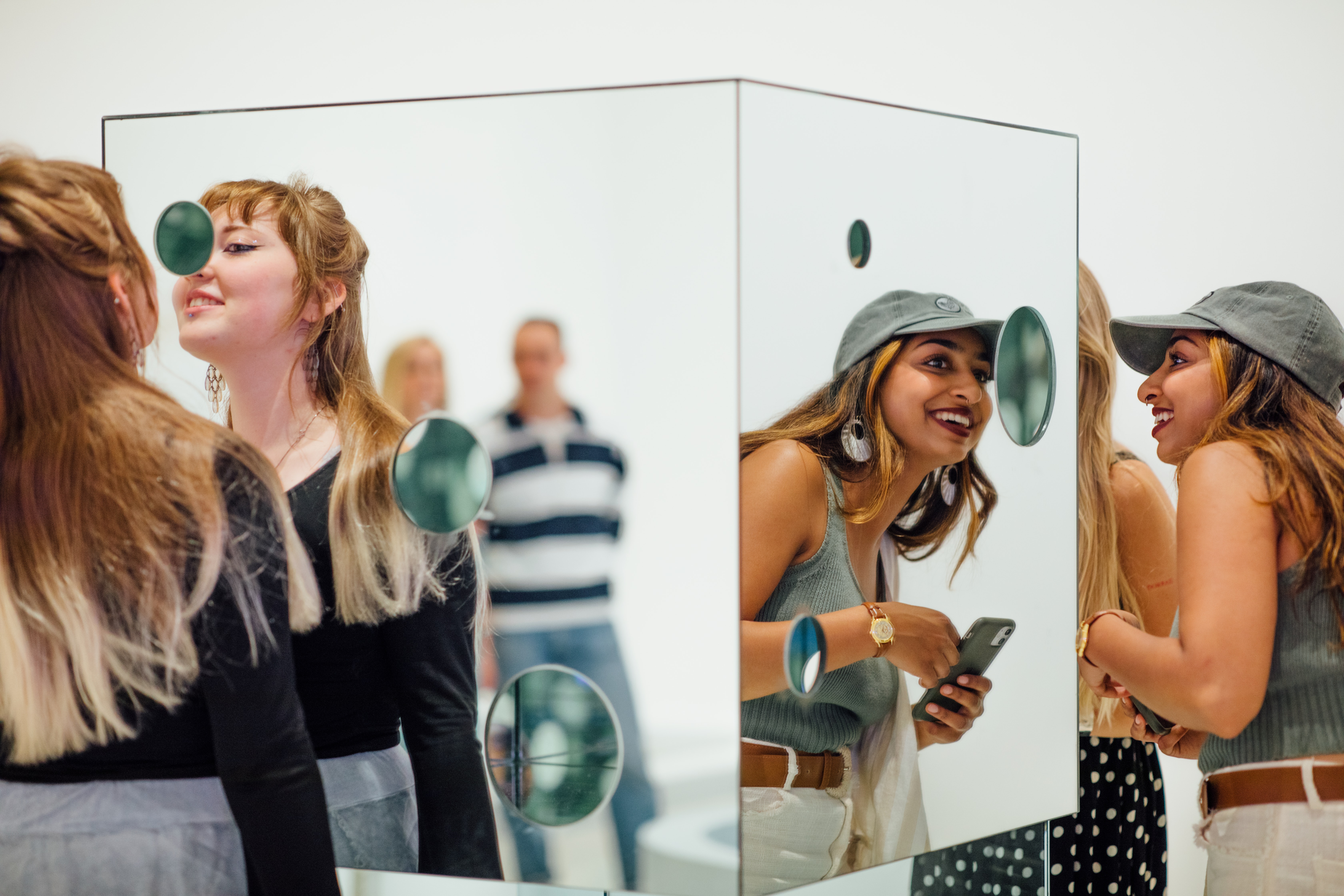 Two adults smile and look into a mirrored art sculpture