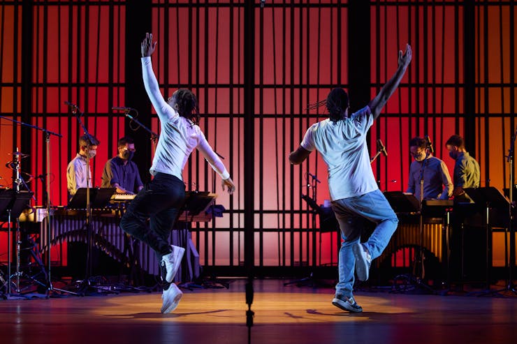 Two men dancing in foreground with four musicians in background on red