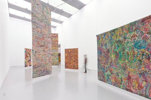 A person walks through a gallery where large, colorful textile artworks hang