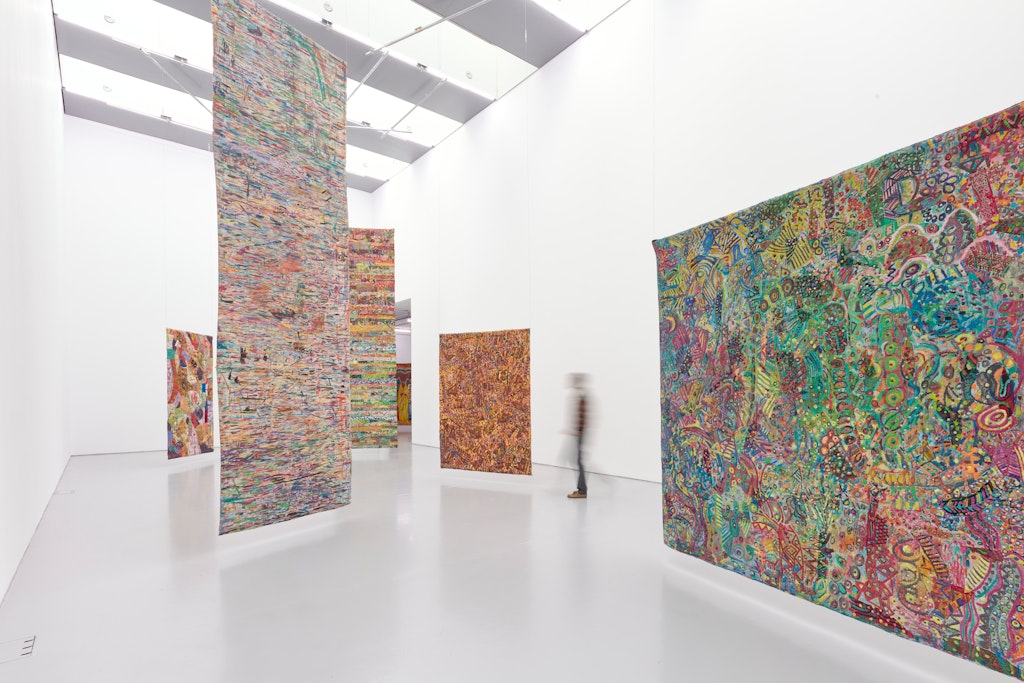 A person walks through a gallery where large, colorful textile artworks hang