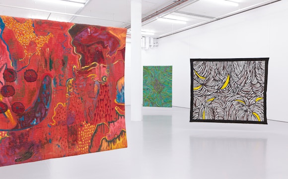 Large, colorful textile works hang in a large white art gallery.