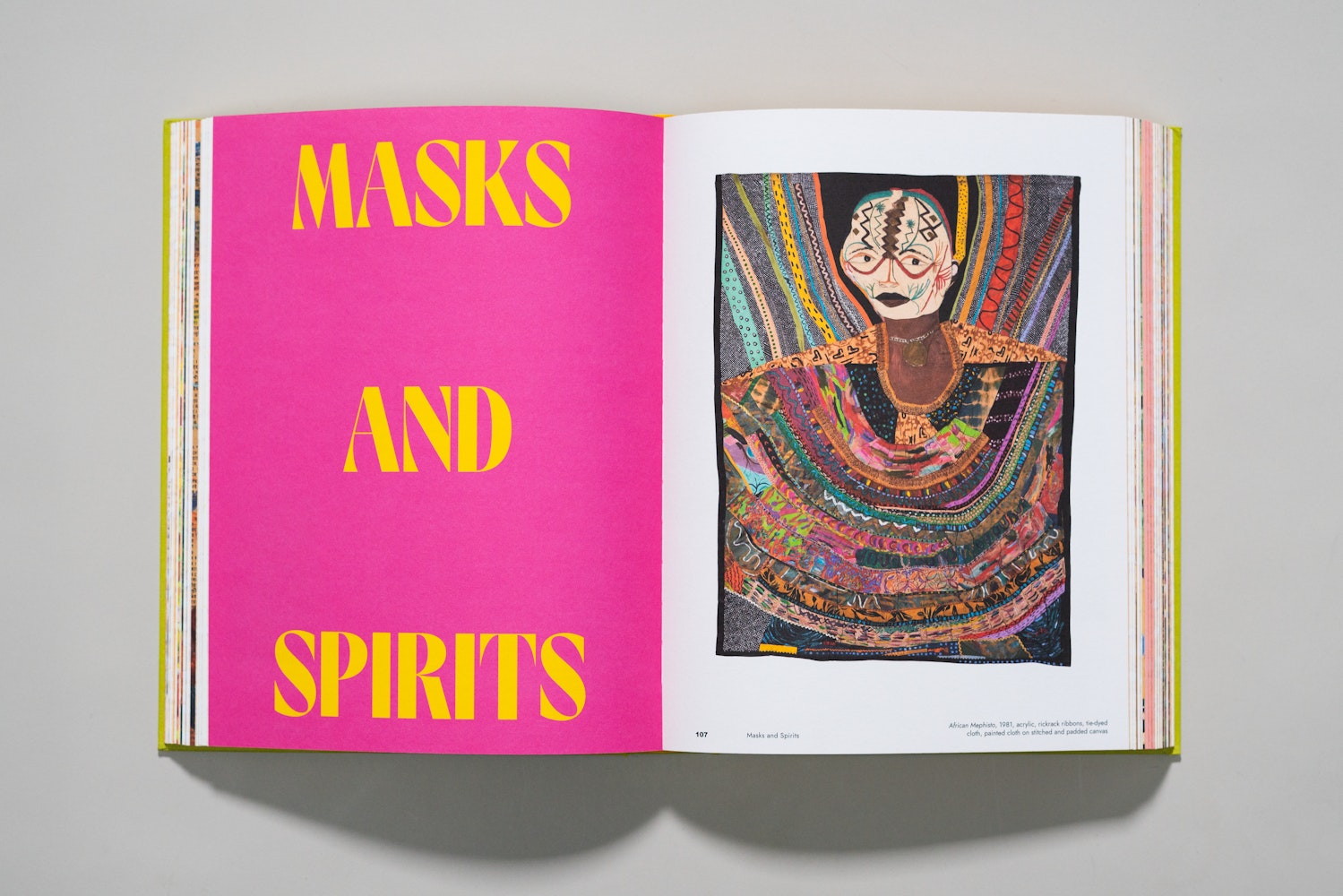 Spread of a large art book is open to a page of an essay with the title Masks and Spirits.