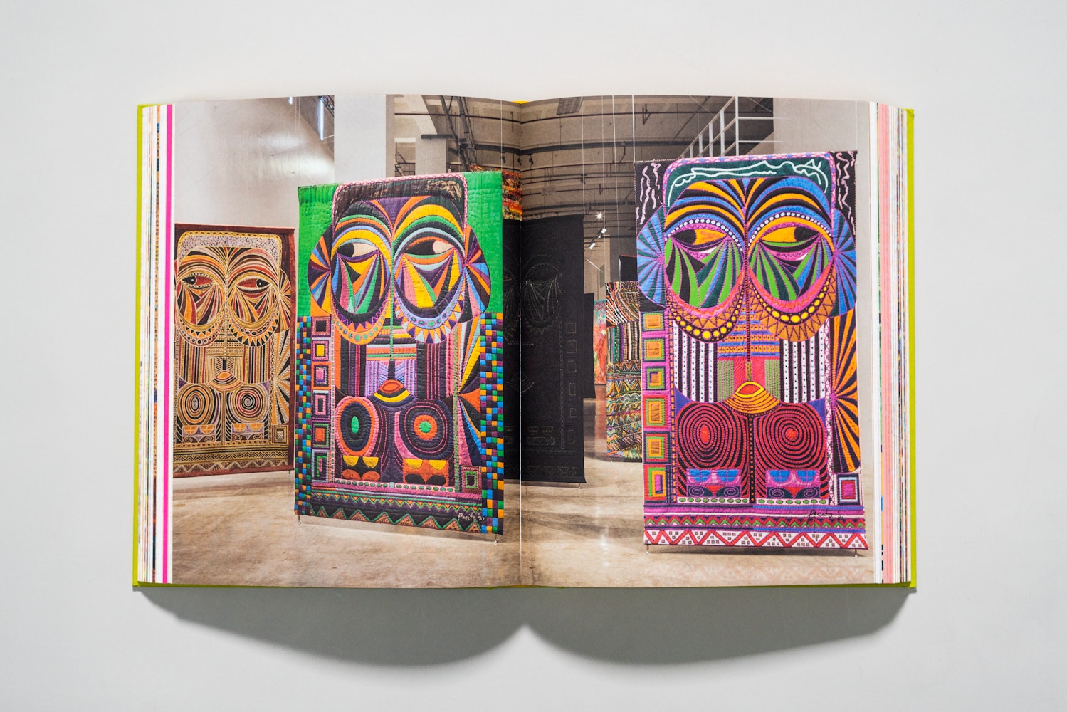 Spread of a large art book is open to a page of a colorful paintings haning in a gallery.