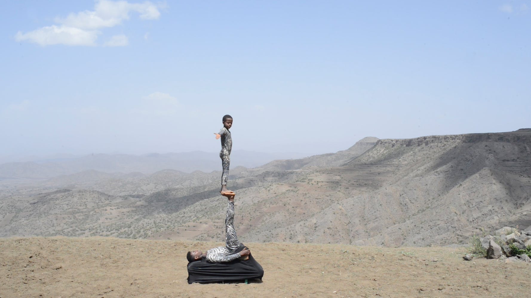 Image of one boy standing on another in the desert