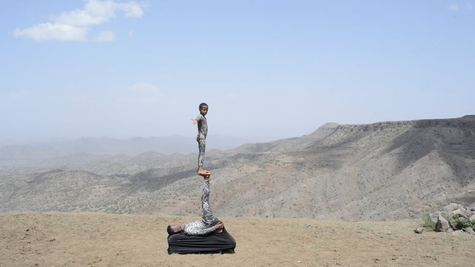 Image of one boy standing on another in the desert