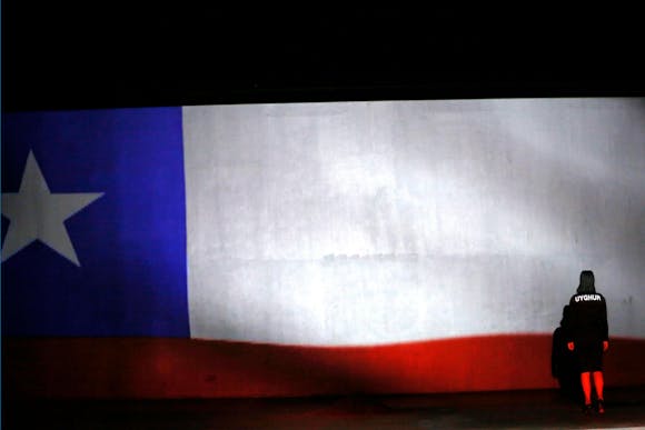 A woman stands on stage with a large large projected over her.