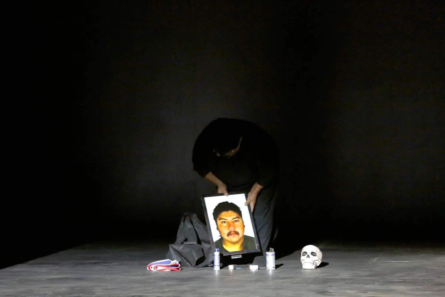 A woman on a dark stage places a photo of a man next to a skull and a folded Chilean flag.