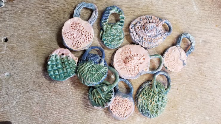 Ten rough-hewn ceramic cameos by Donna Ray with texture reminiscent of braids in blues, greens, and taupes.