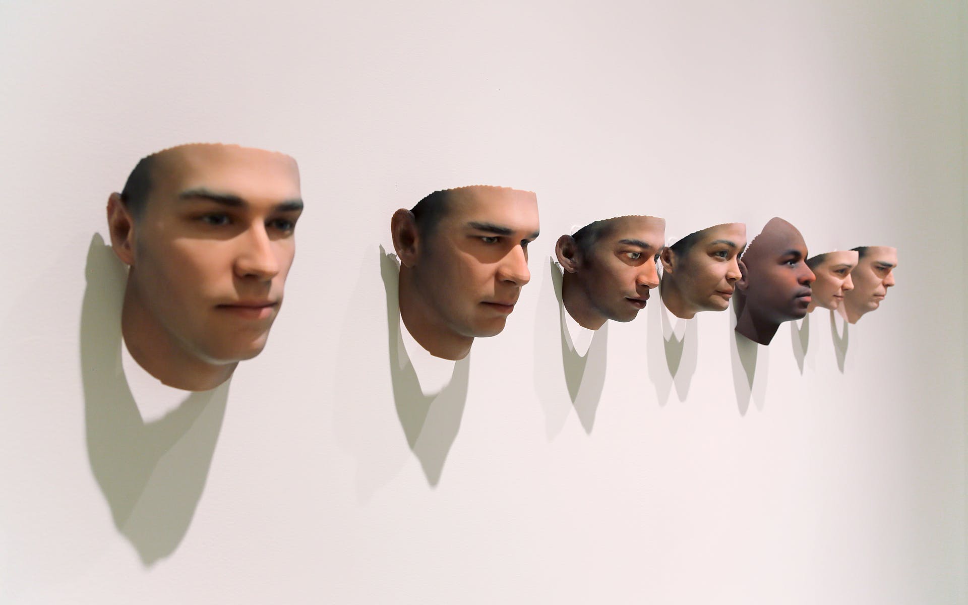 Seven 3d printed human heads mounted to a wall