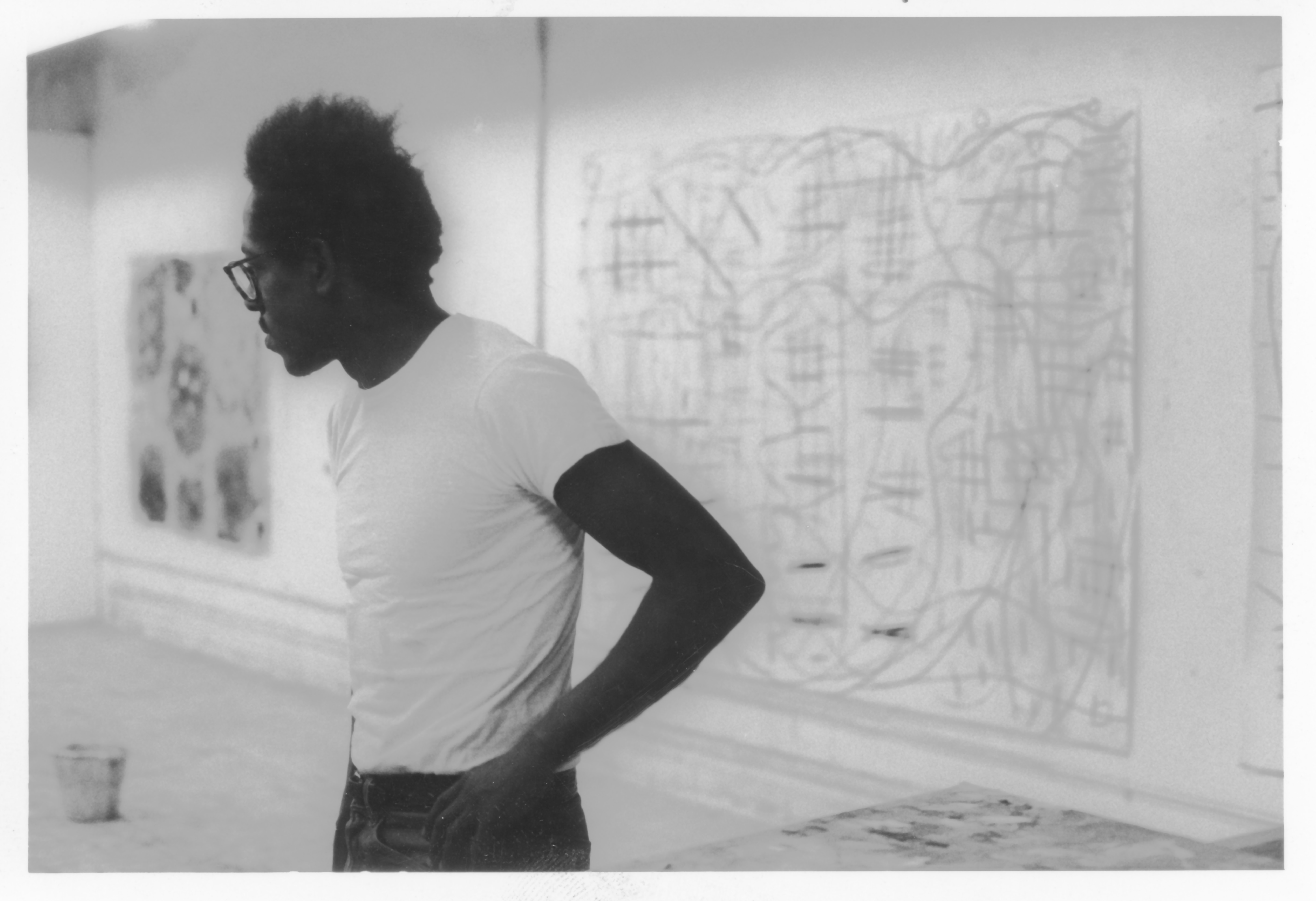 A young black man standing in front of large drawings hung on the wall.