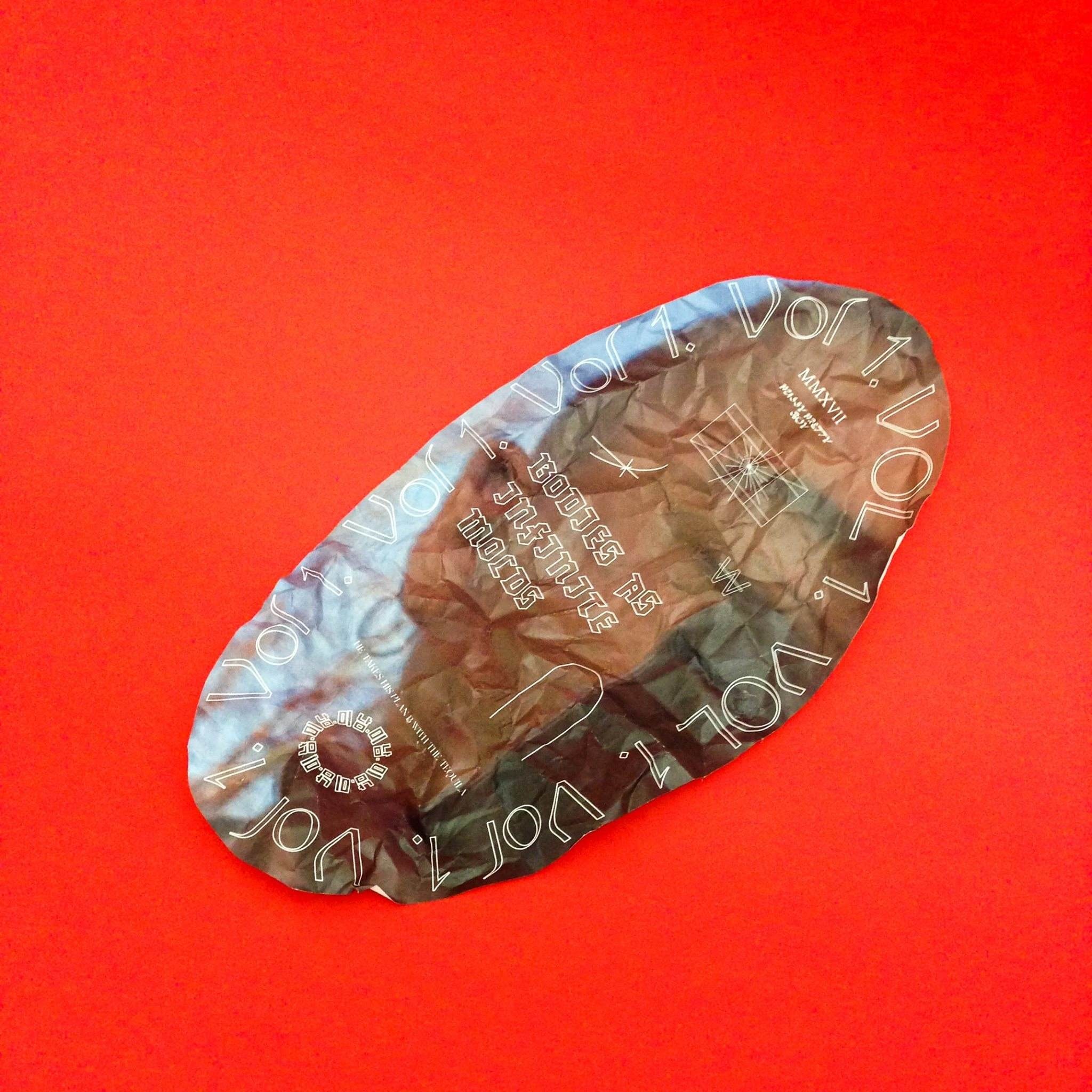 Image of crumpled paper in an oblong shape with complex typography on red background