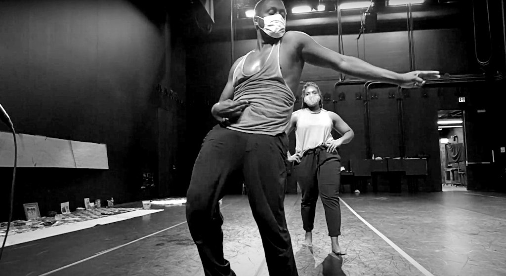 A black and white image of two dancers wearing PPE masks rehearsing in a studio.