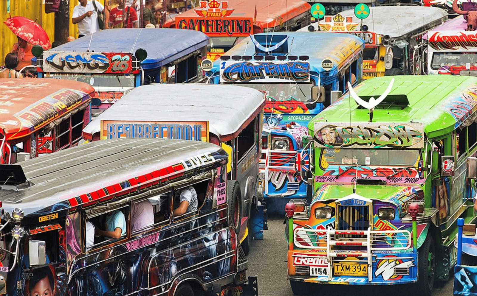 Many buses painted with lots of images and colors drive down a road.