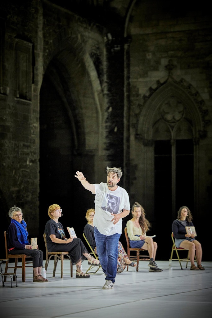 A photograph from behind a white stage with seated performers.