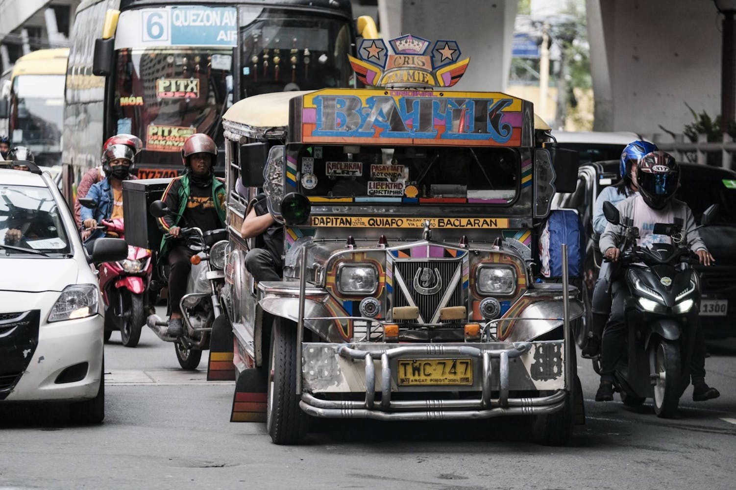 A bus painted with many images and colors drives down a road.