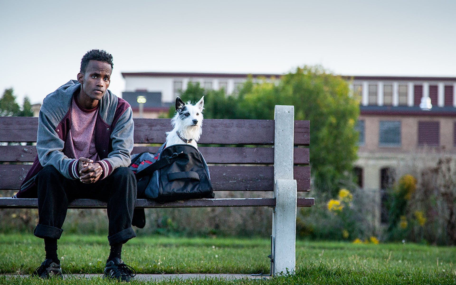 Man sitting on bench with dog and gym bag.