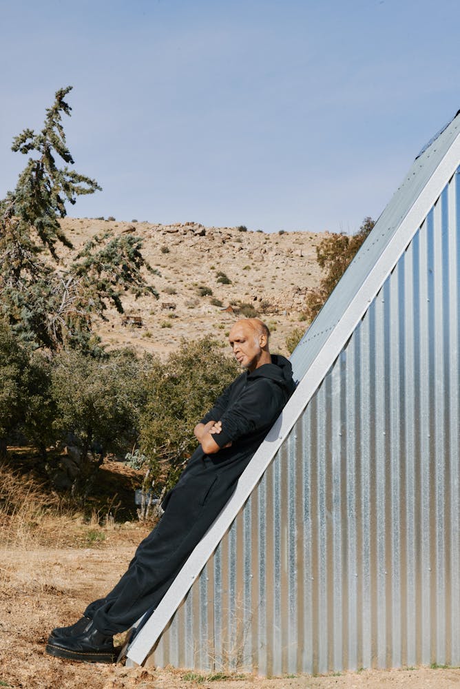 A person with medium skin lays back on a slanted metal roof, arms crossed.