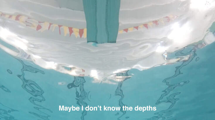 Point of view of someone looking up at a diving board while underwater at an indoor pool.