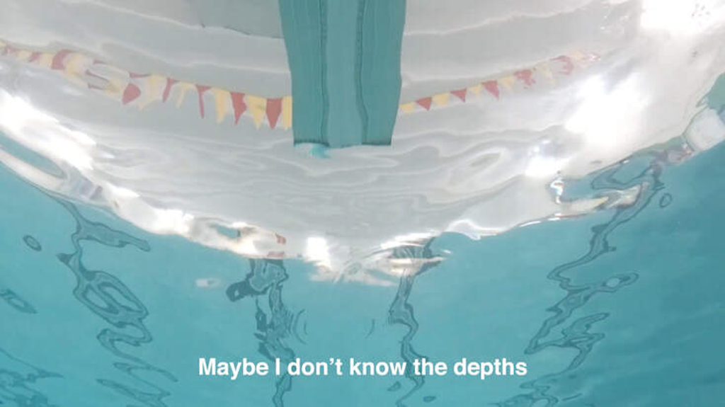Point of view of someone looking up at a diving board while underwater at an indoor pool.