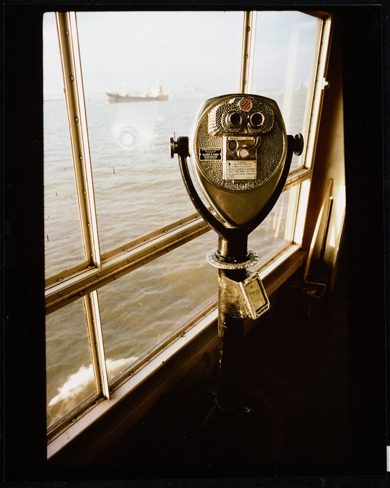 A metal viewing station sits by a window looking out at the ocean.