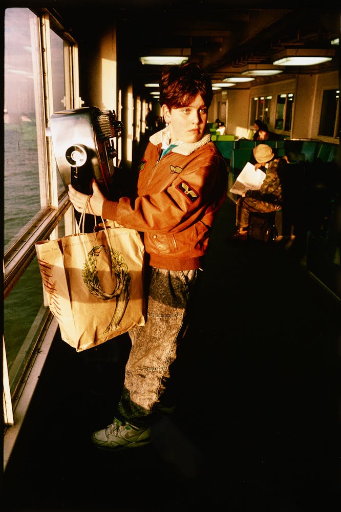 A young adult stands at a viewing station sits by a window looking out at the ocean.