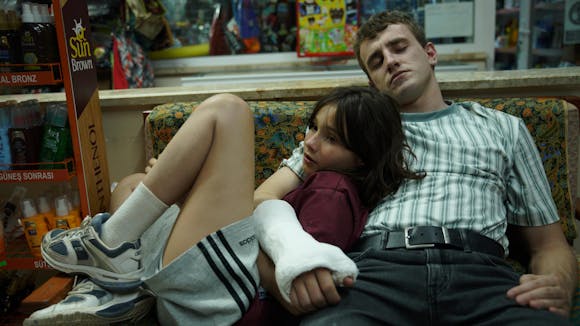 A young person leans up against a man with his arm and hand in a cast as they sit on a couch.