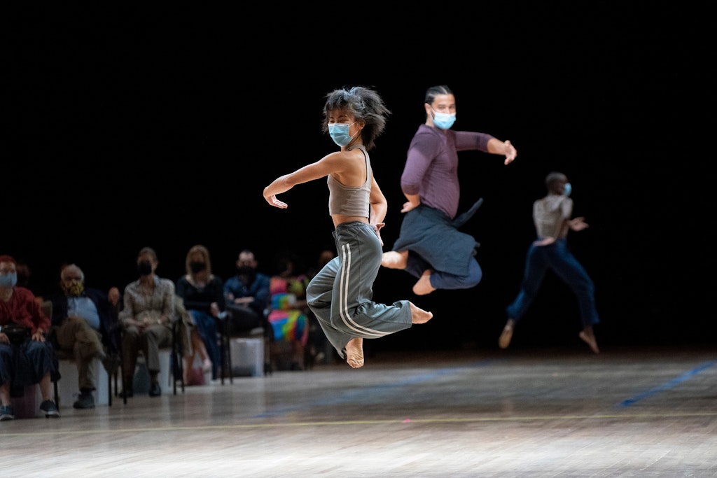 Two dancers mid-leap with audience members in background