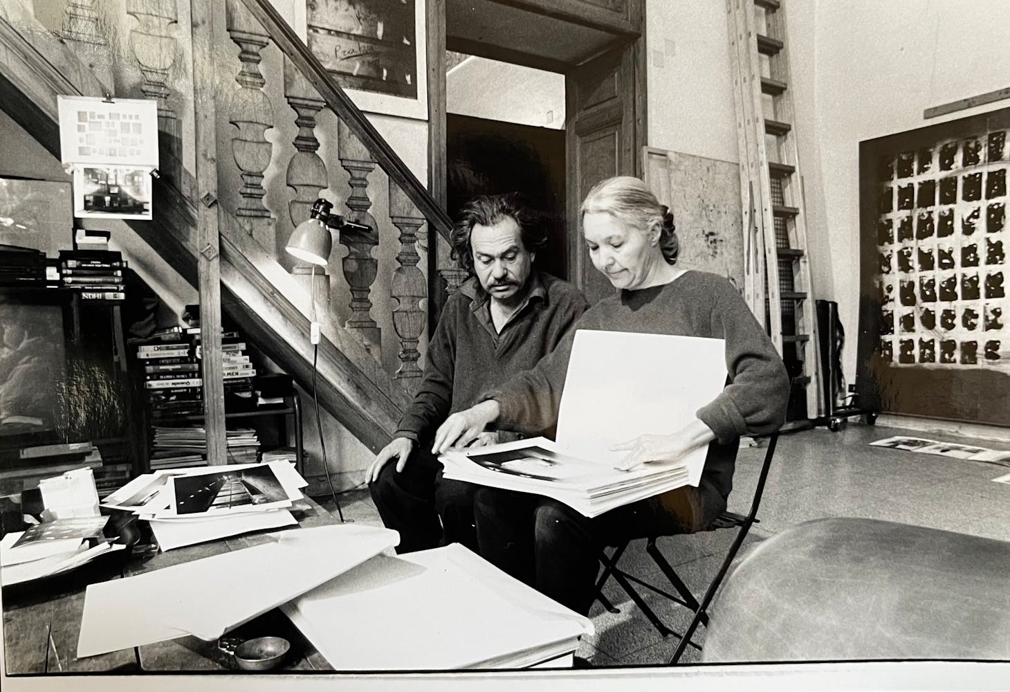 A man and a woman sit in an artist studio looking and photographic prints.