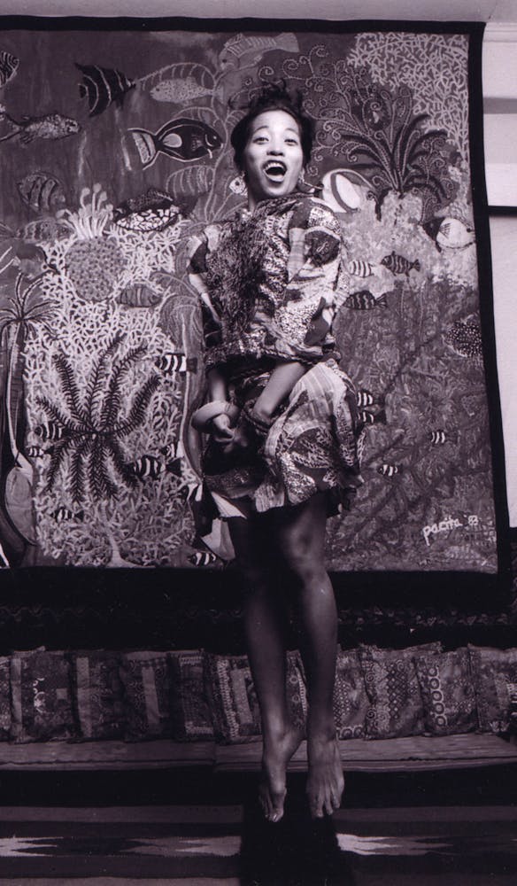 An adult jumps in the air in front of a painting while laughing at looking at the viewer.