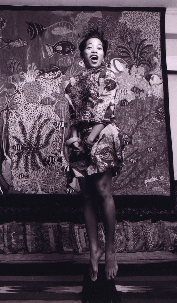 An adult jumps in the air in front of a painting while laughing at looking at the viewer.