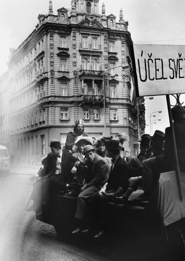A group of men ride on the back of a truck through a European city street.