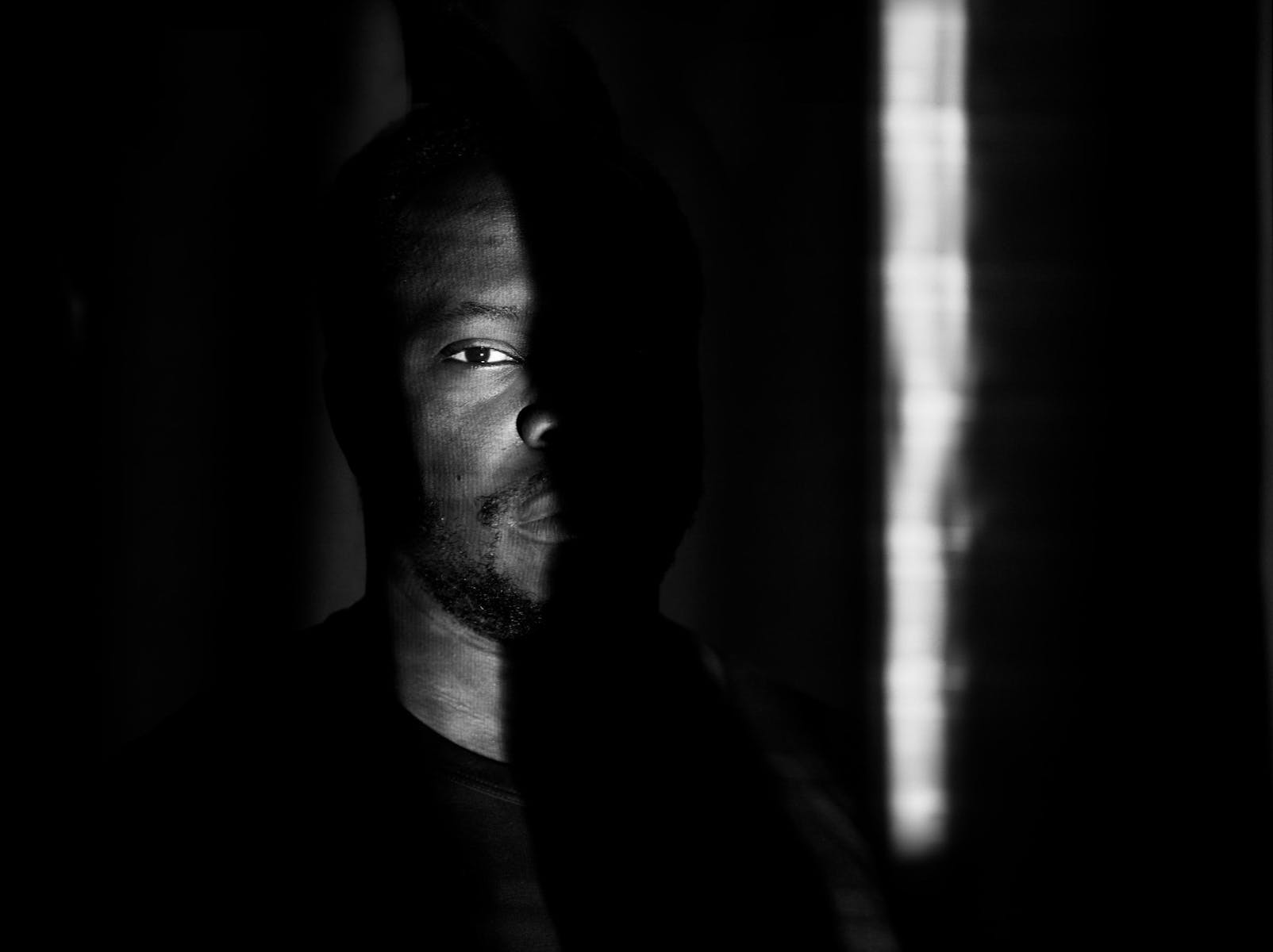 Black and white portrati of a man standing in shadows.