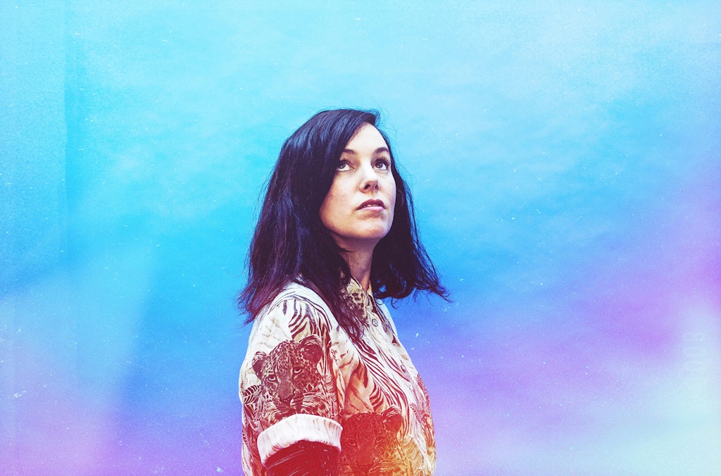 Woman in colorful shirt standing in front of a light blue and purple background.