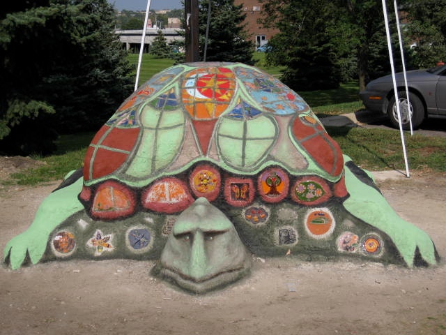 Sculpture of a turtle painted onto rock. The shell and front of the turtle are painted in different colors with symbols and small illustrations.