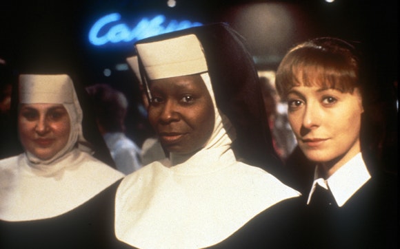 Three women in nun habits look at the viewer while standing in a nightclub.