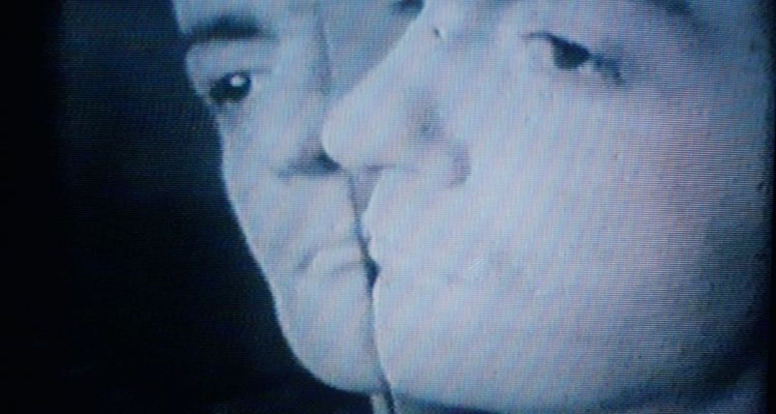 Screenshot of an adults face close up to a mirror, reflecting their image.