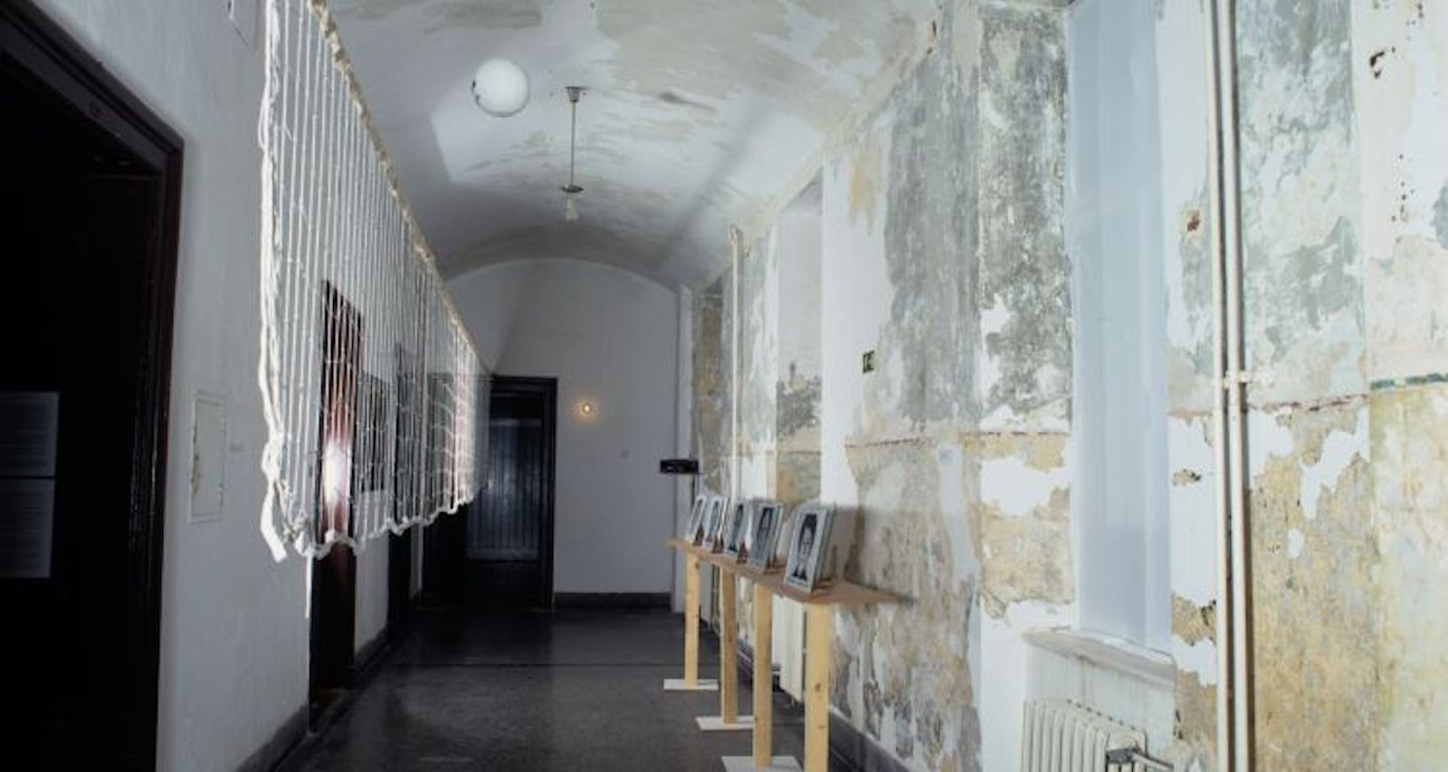 A gallery space with worn walls and images on wooden podiums along the wall.