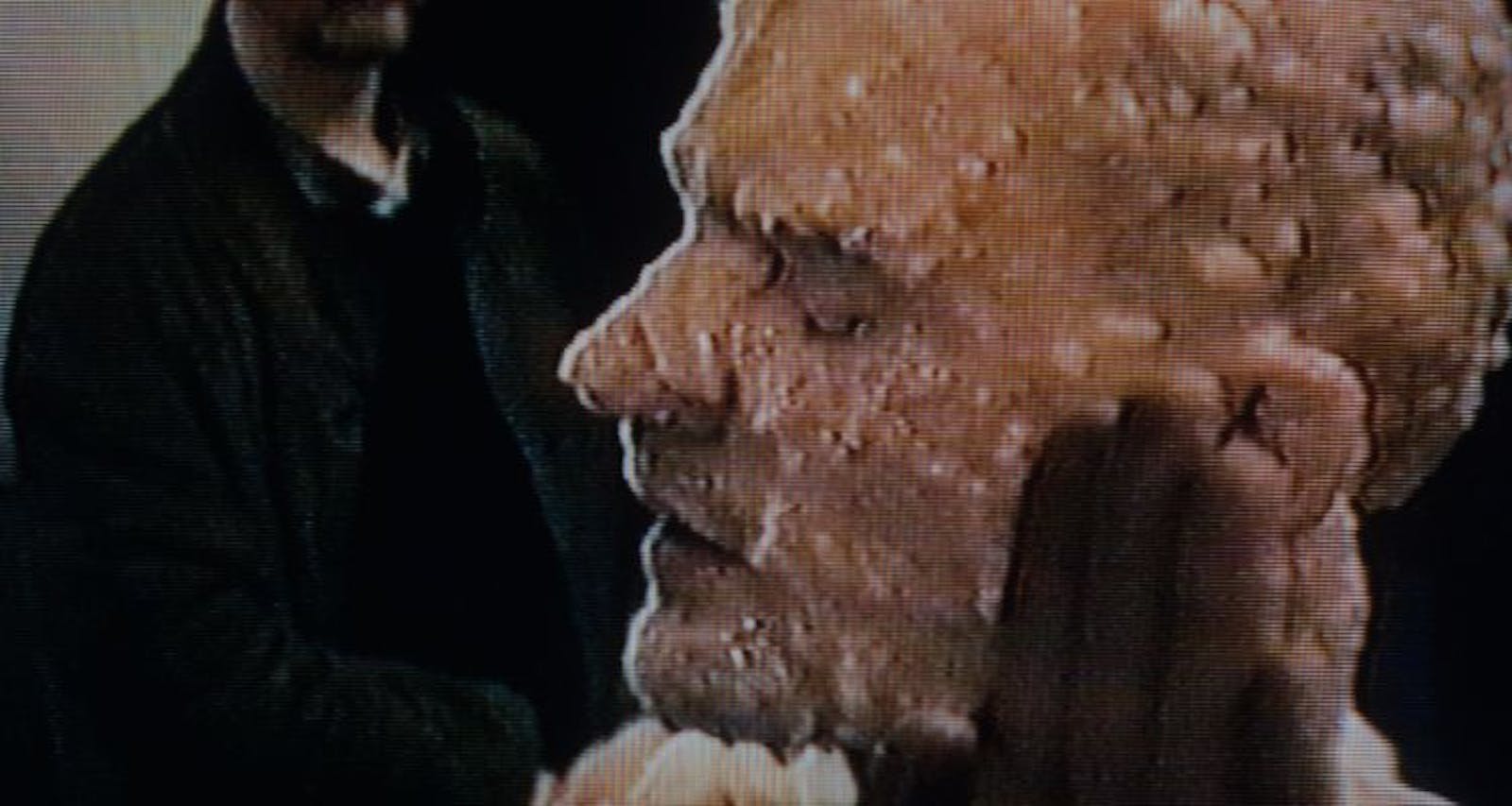Screenshot of an adult with something covering their face and head.