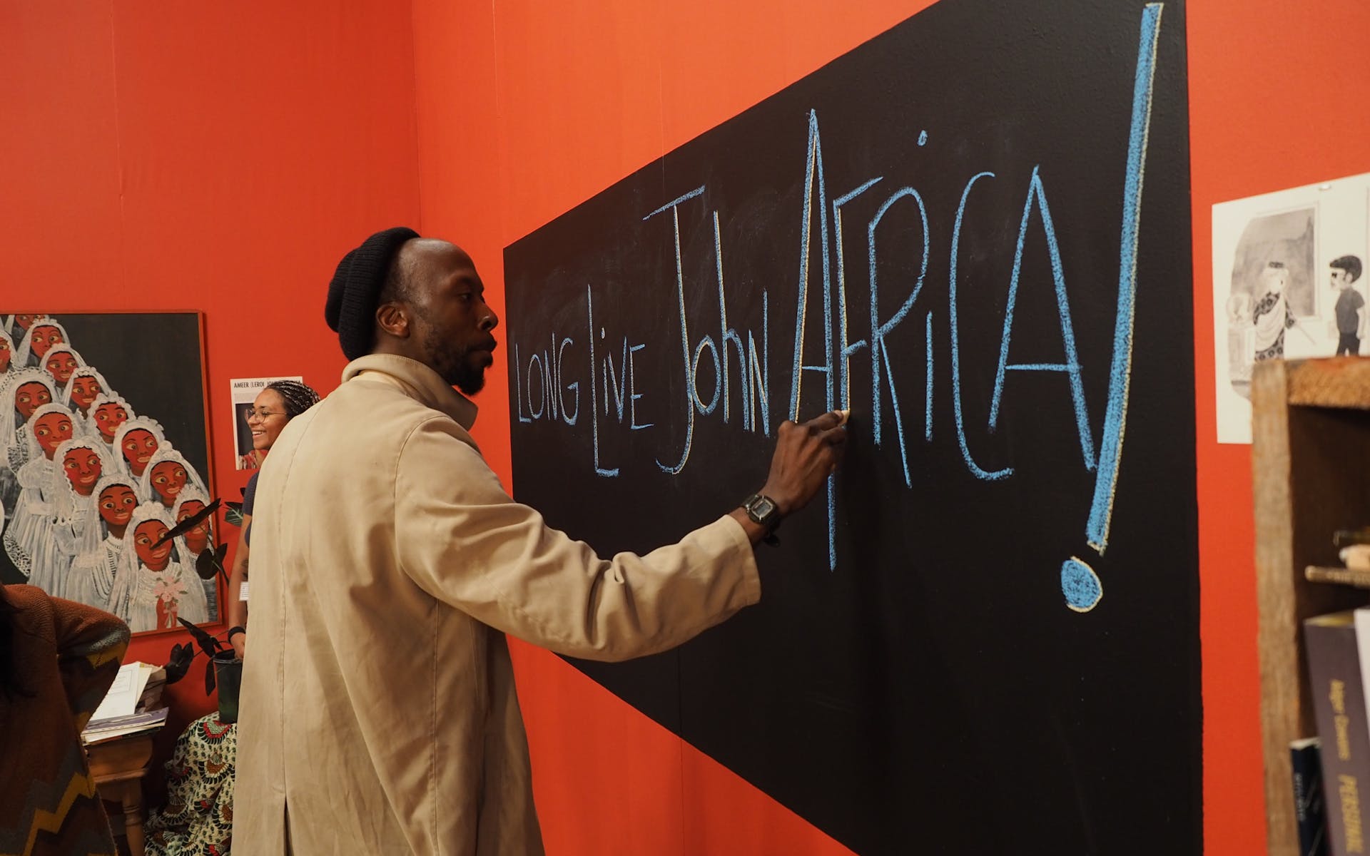 A Black man write on a chalkboard a message that reads Long Live John Africa.