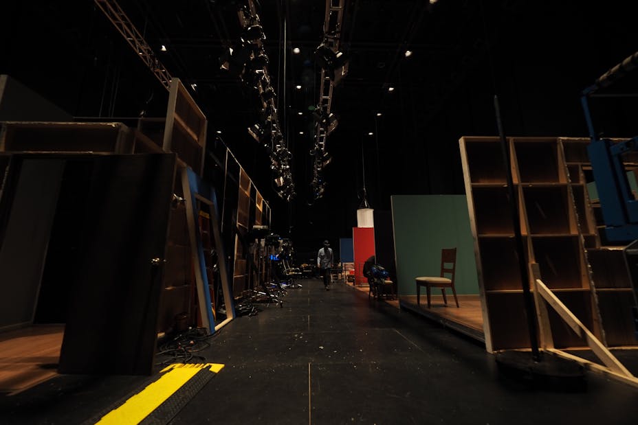 A man walks through the darkened backstage of a theater.
